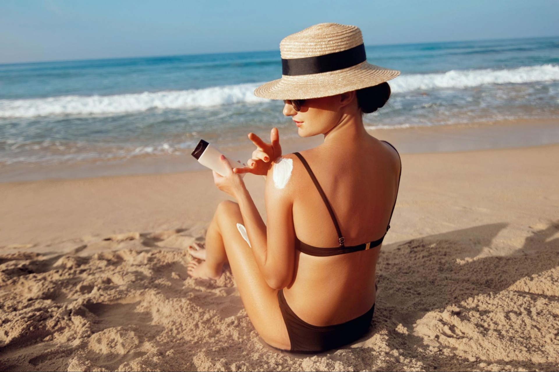 A woman reapplies sunscreen on her shoulder while tanning on the beach 