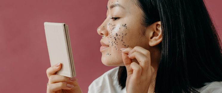 A woman looking in a mirror while peeling off a clear mask