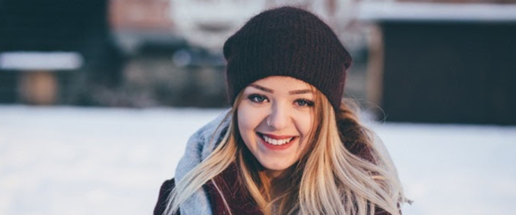 A smiling, beautiful woman dressed in winter clothes out in the snow