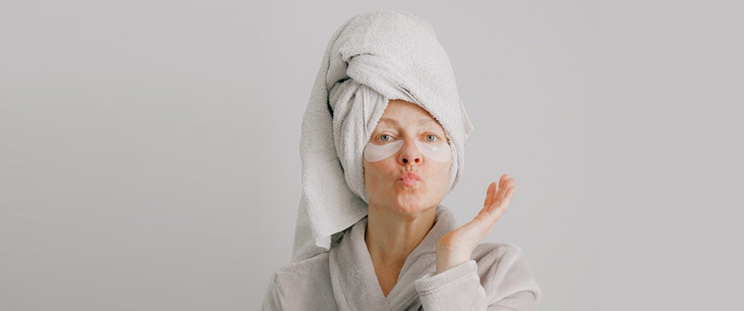 Older woman pouting for the camera dressed in a robe wearing under eye masks