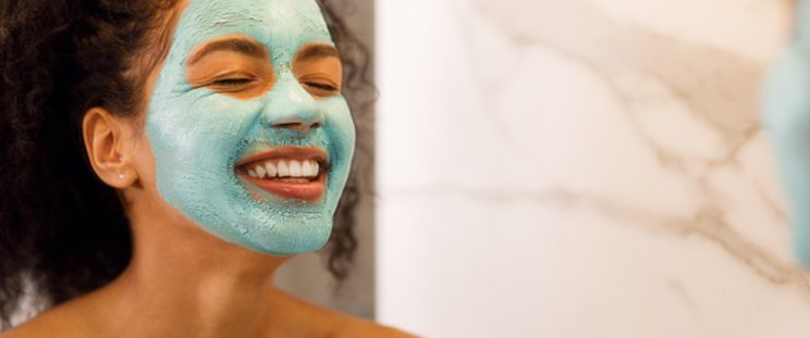 Beautiful woman smiling in a mirror with a skincare mask on