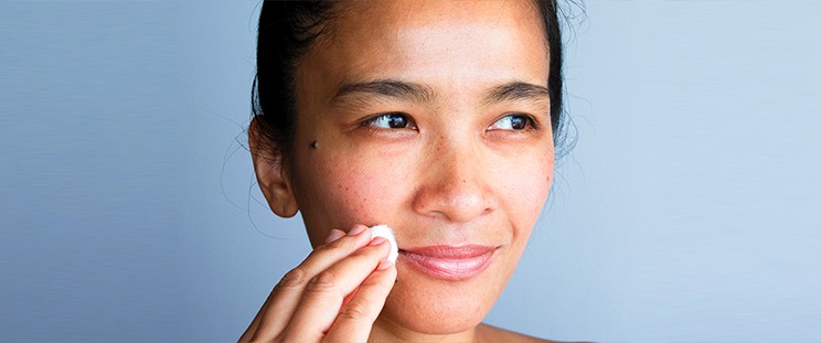 A woman cleaning her face with a cotton pad
