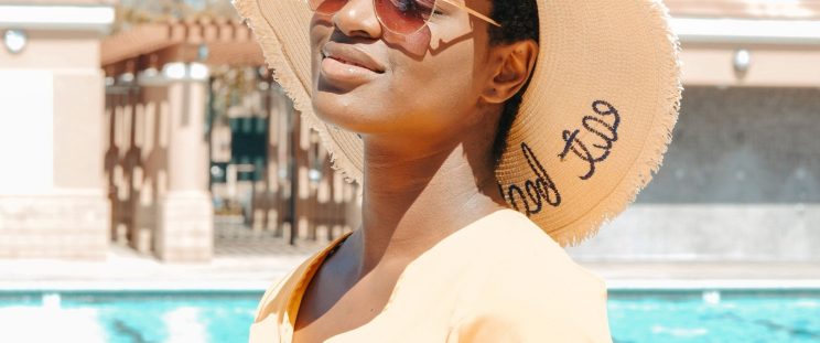A woman standing by a pool with a hat and sunglasses on