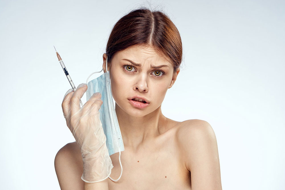 A woman holding up a syringe and a face mask