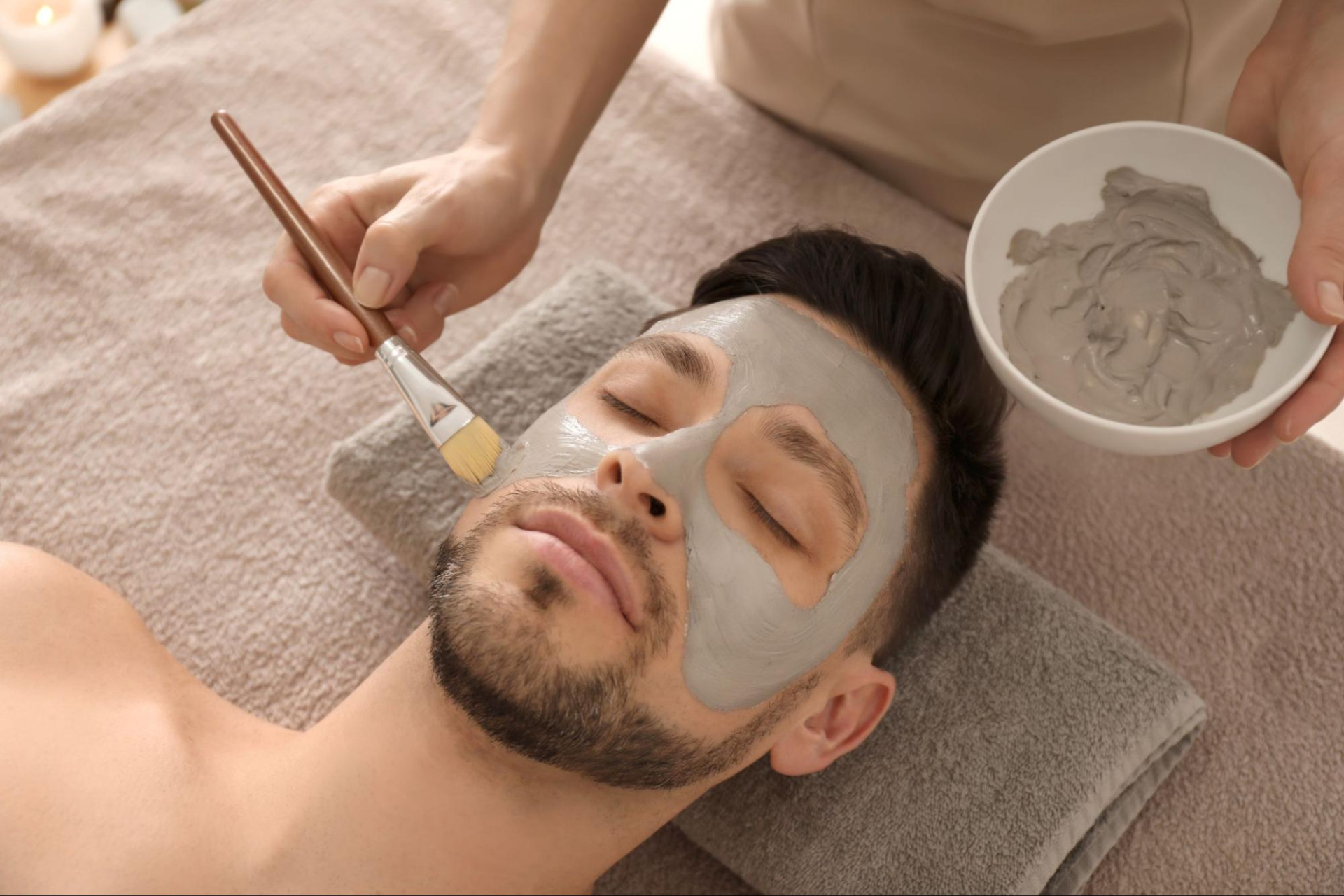 An aesthetician applies a mask on a patient’s face with a brush