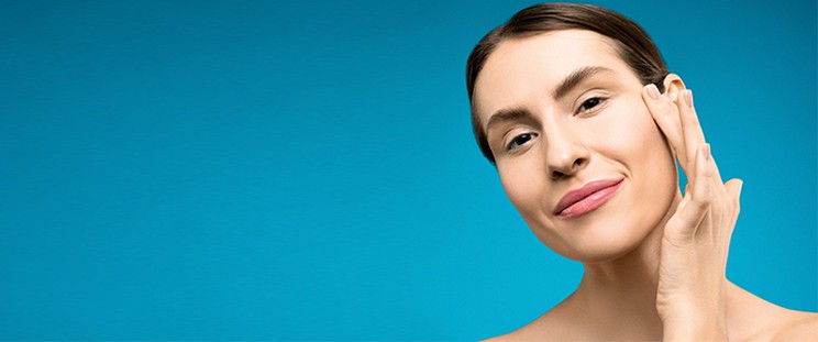 A smiling woman lightly touching her cheek a few months after undergoing microneedling