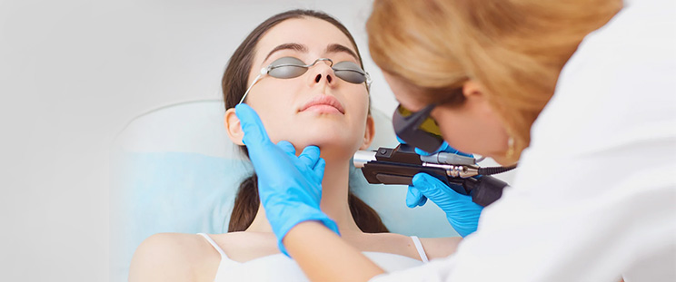 A skin expert performs laser skin resurfacing on a young woman to treat her acne scars and blemishes