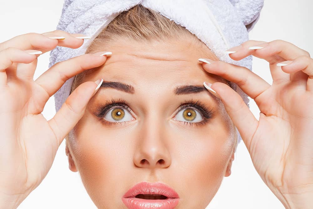 a woman wearing a towel on her head stretching her forehead wrinkles 