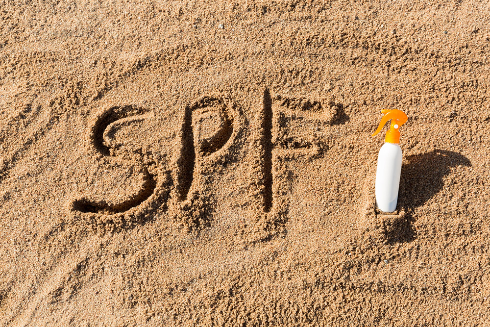  The acronym “SPF” written in the sand next to a bottle of sunscreen 