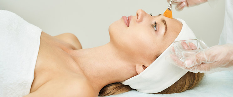 An aesthetician puts a chemical peeling agent on the forehead of a patient