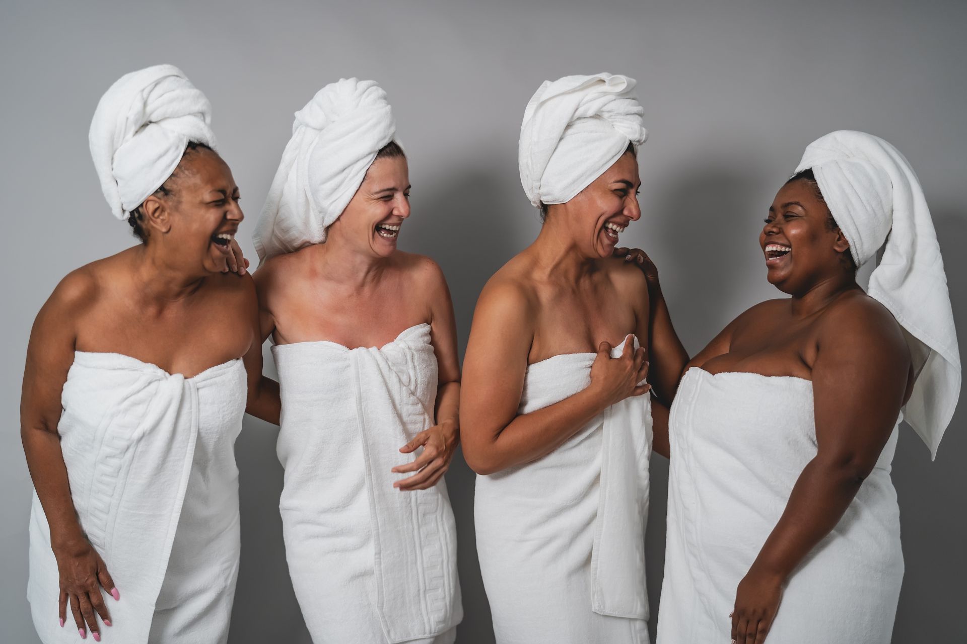 A group of four women in bath towels, smiling and laughing with each other