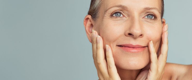 An older woman touching her face, smiling, and posing for the camera