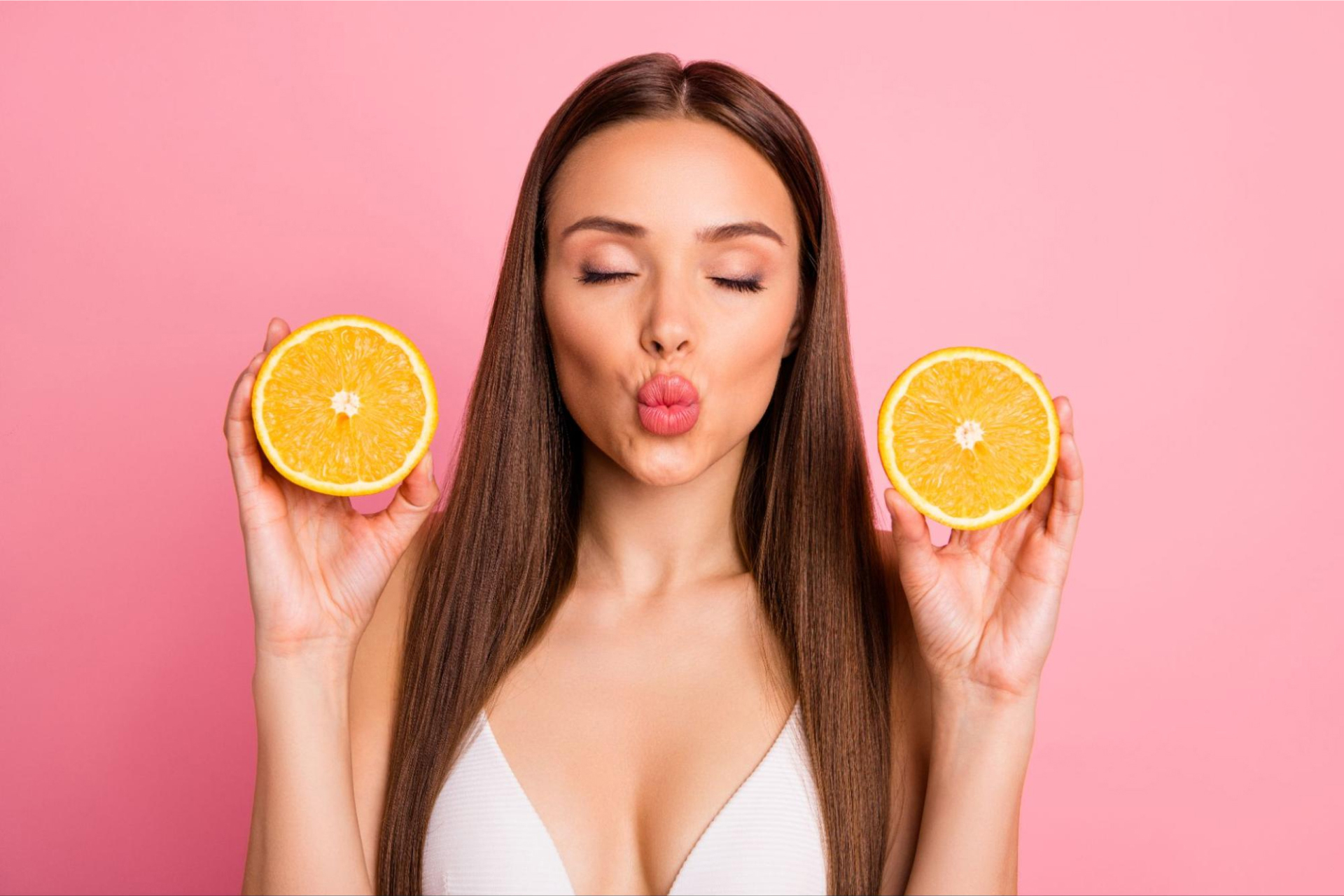 A woman with full lips closes her eyes while holding two slices of orange