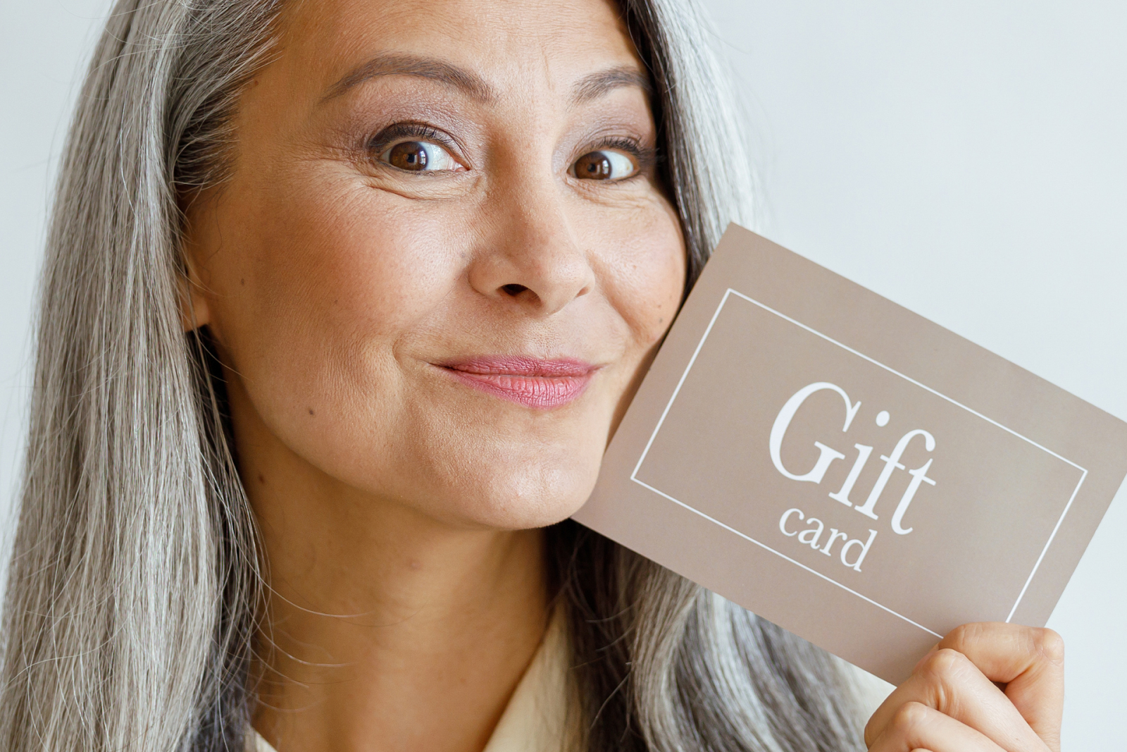 A woman smiles as she holds a gift card for APT Medical Aesthetics
