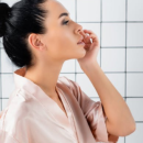 A woman applying retinol on her face as she looks in the mirror