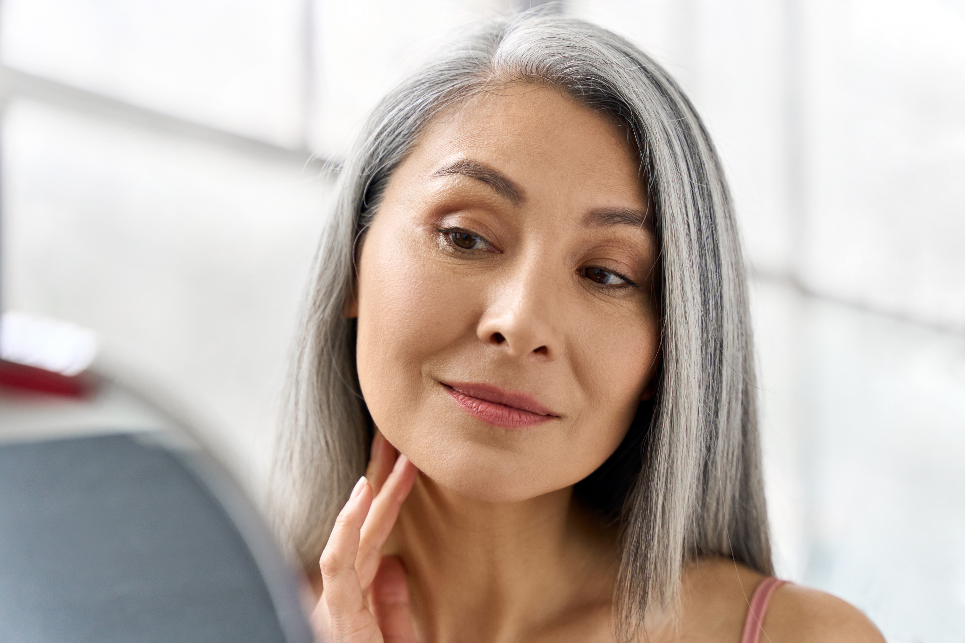 a woman looking in the mirror at her aging skin 