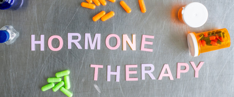 Pills and pill bottles surrounding the words “hormone therapy” atop a gray surface.