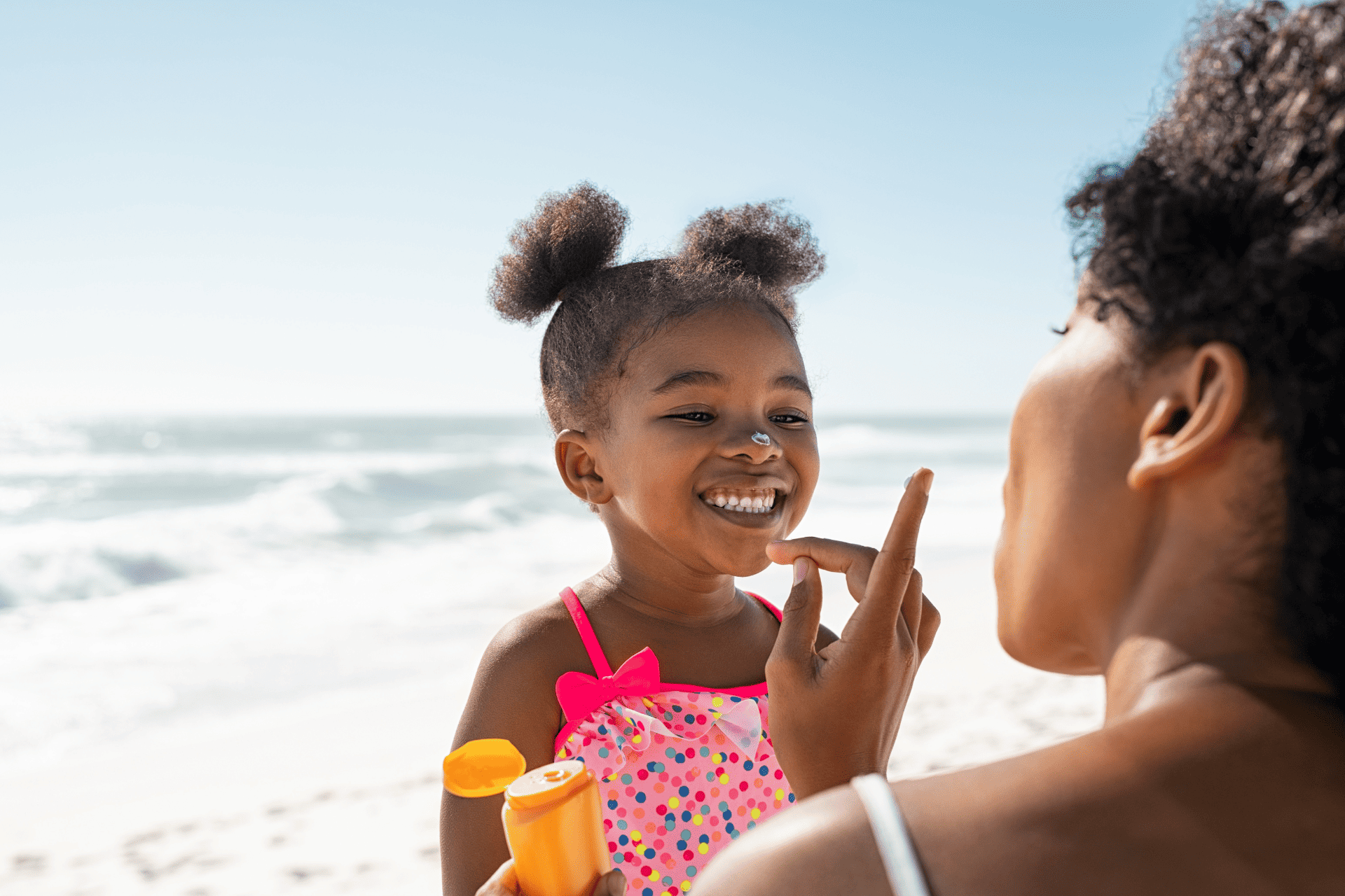 a mother applying sunscreen on her daughter at the beach
