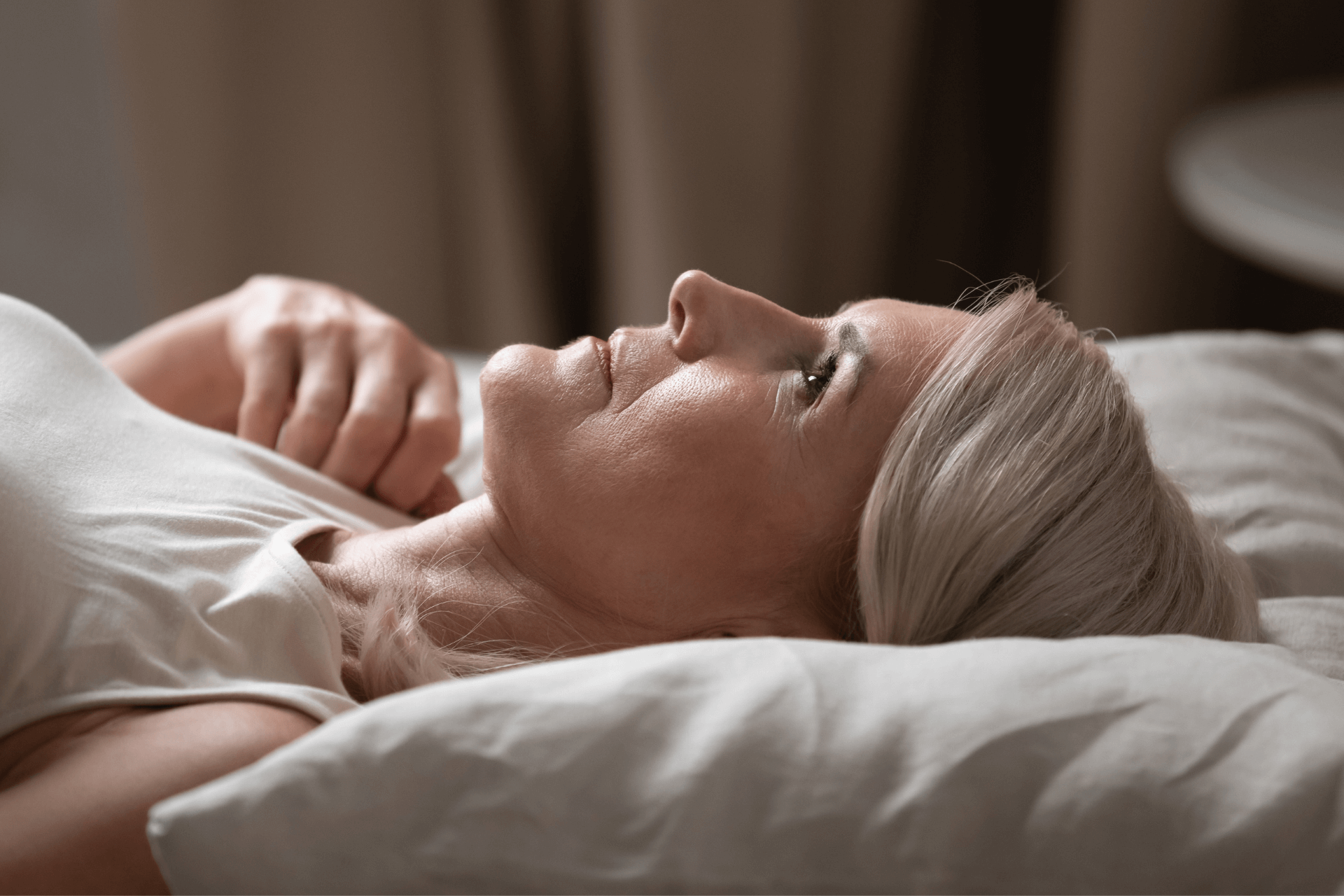 an older woman lying in her bed, staring up at the ceiling 