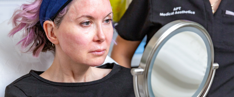 An APT Medical Aesthetics patient checking her face in the mirror after a collagen for face treatment